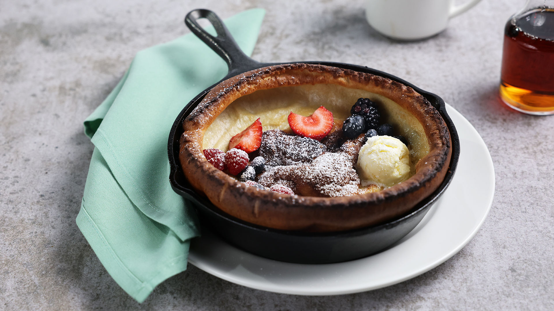 Dutch berry pancake in a cast-iron skillet with berries, butter and powdered sugar