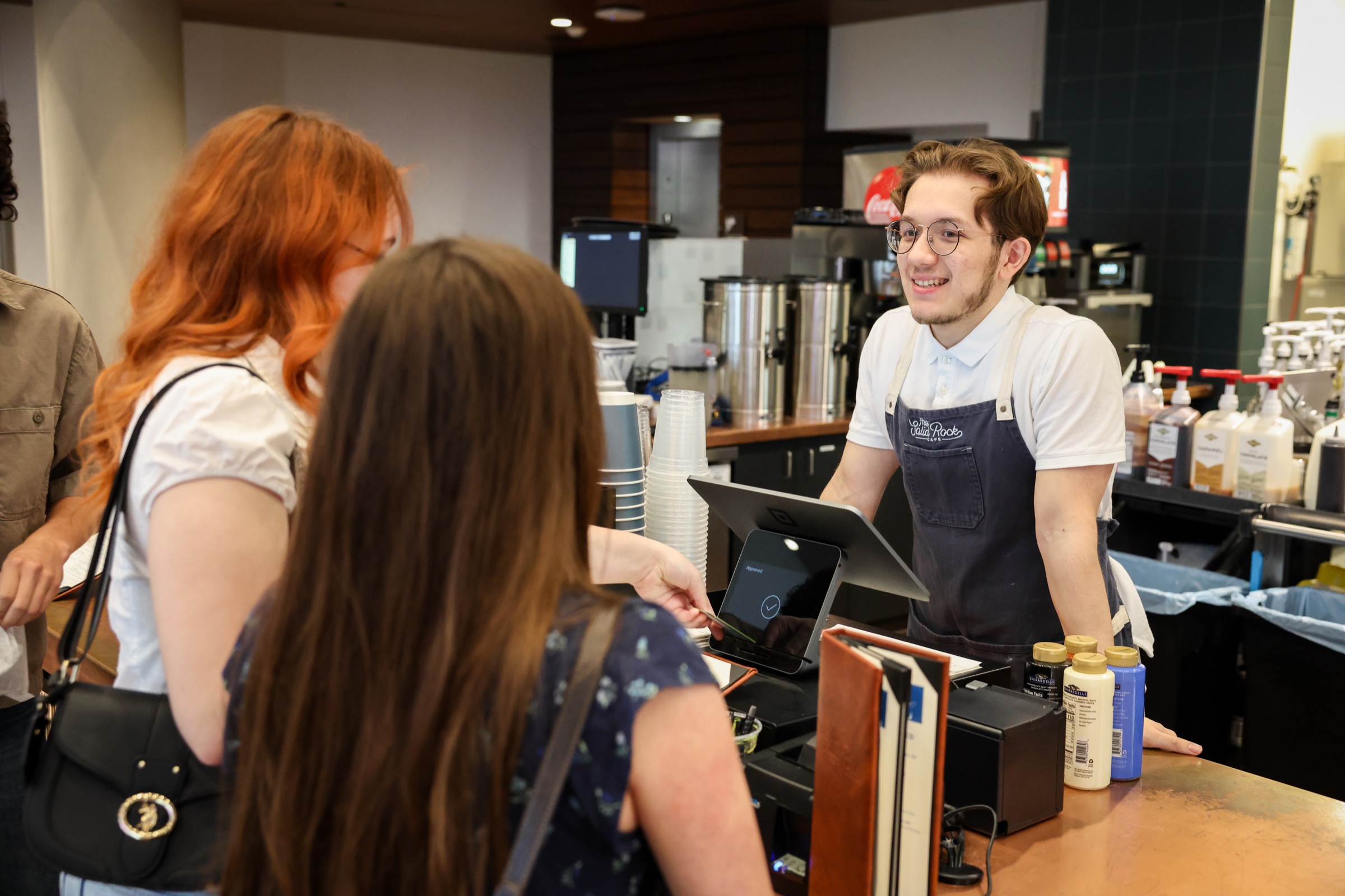 A barista greeting guests at the café counter