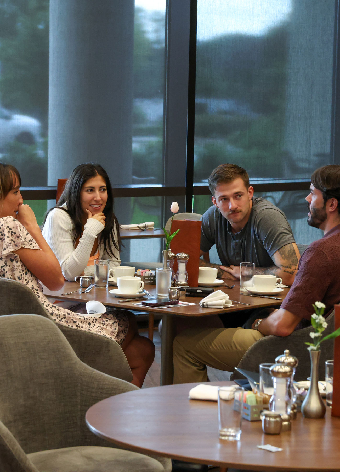 Friends gathered around a café table with coffee, talking by the windows